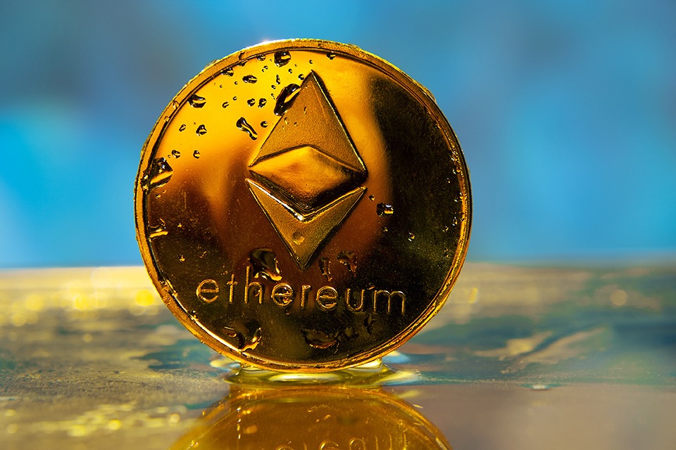 A gold ethereum coin adorned with the UKCrypto logo sits on top of a blue blockchain background.