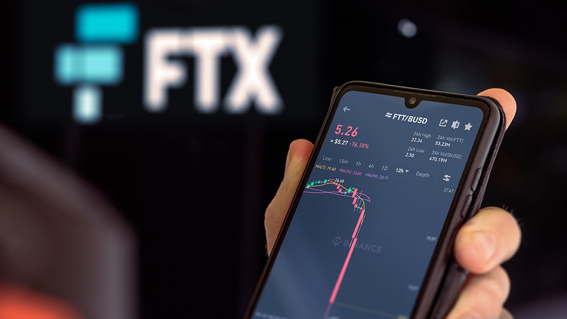 A person holding up a phone with the FTX logo on it, showcasing the cryptocurrency market and blockchain technology.