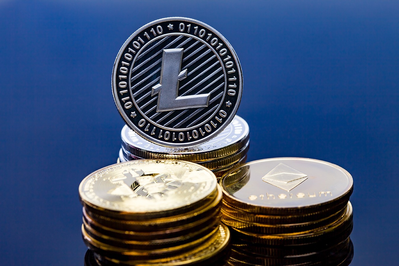 A silver Litecoin LTC on a blue background stacked with bitcoin and Ethereum coins.
