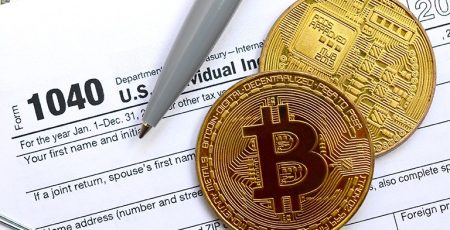 A pen and a bitcoin sit on top of a tax form, showcasing the interaction between traditional paperwork and the digital currency bitcoin.